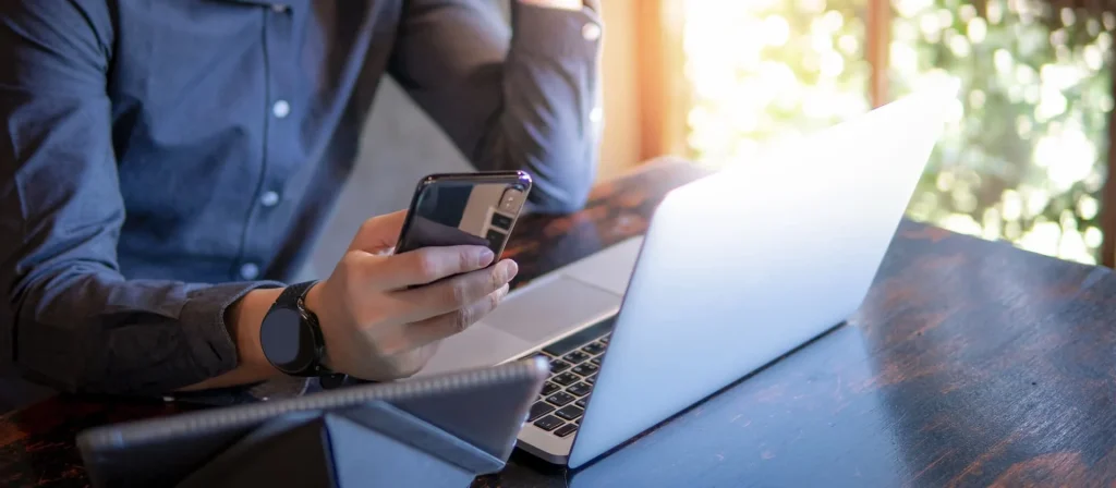 man looking into his phone and an open laptop