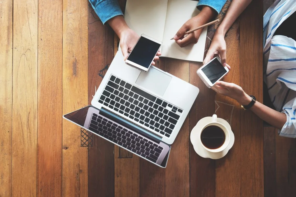 two people working on their phones with a coffee and laptop